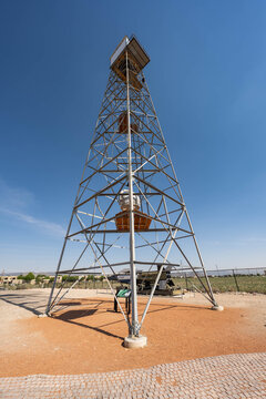 View of a tall, silver observation tower piercing the clear blue sky, standing prominently on a red-brown earth base, reaching high above the landscape, Santa Fe, New Mexico, United States.