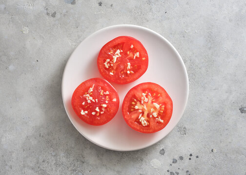 Slices of fresh tomato on a white plate on a light gray surface ready for cooking or eating during daytime