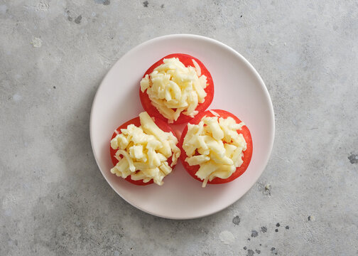 Fresh tomatoes topped with cheese on a plain plate in a kitchen setting during daylight