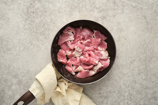 Slices of raw pork meat in a skillet on a kitchen counter during meal preparation