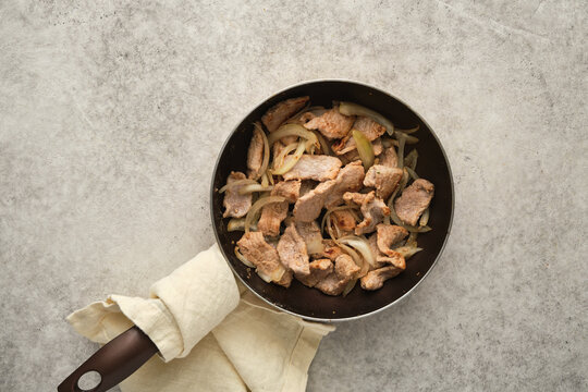 Cooked meat and onions in a frying pan on a light countertop in a kitchen