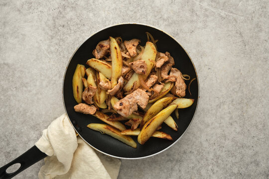 Chicken and potato stir fry in a pan on a gray surface with a towel