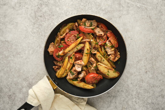 Chicken and potato dish with tomatoes prepared in a frying pan in a kitchen setting during day time