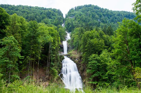 Breathtaking multi-tiered Giessbach waterfall cascading through a lush green forest in the Swiss Alps, featuring a scenic wooden bridge.
