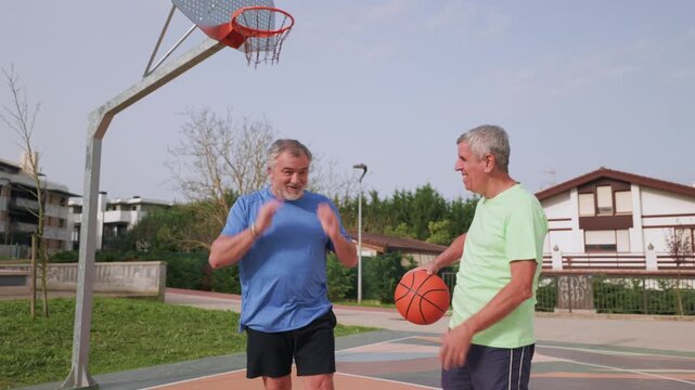 Two active senior friends joking and laughing after a failed basketball shot on an outdoor court, showing a healthy and happy lifestyle and the importance of friendship in old age