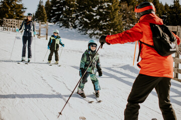Naklejka premium Family enjoys skiing together on snowy slope in winter sun