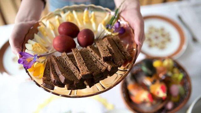 Close-up of traditional Easter plate full of coloured eggs and bread slices. Table decoration with flowers. Easter celebration.