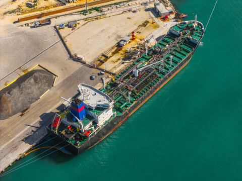 Aerial view of a massive tanker ship, a titan of steel and color, contrasts with the serene turquoise harbor waters, docked at the industrial pier, Ortona, Abruzzo, Italy.