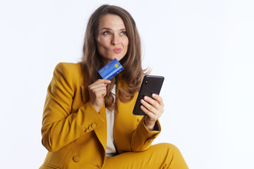 Naklejka premium A middle-aged businesswoman in a yellow suit holds a credit card and smartphone with a playful, upward glance, representing the ease and joy of modern digital finance.