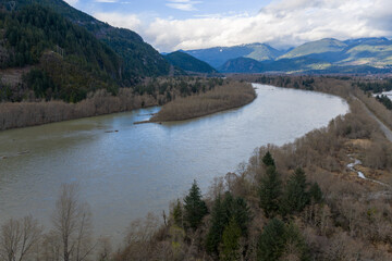 Fototapeta premium Wide Meandering River Through Forested Valley With Mountains and Overcast Sky in BC, Canada