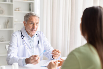 Obraz premium Senior male doctor explaining treatment plan to female patient during clinic consultation. Healthcare professional giving advice and discussing healthcare options