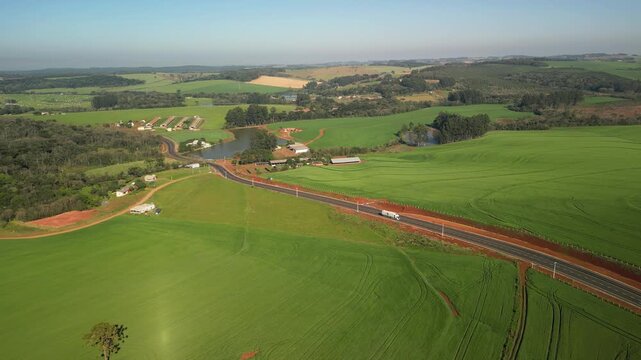Caminh�o transitando em rodovia em meio a campos de cultivo. C�u azul.
