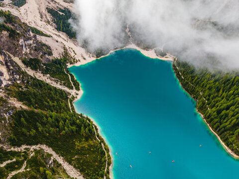 Aerial view of emerald waters meet rocky cliffs and verdant forests beneath a blanket of clouds, Lago di Braies, Prags, Trentino-South Tyrol, Italy.