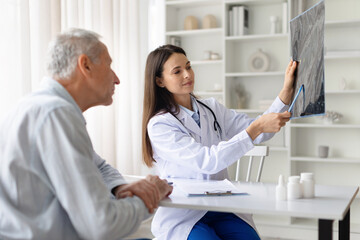 Female doctor showing medical x ray image to senior patient in clinic office. Healthcare professional explaining diagnostic results and treatment options during medical consultation © Anastasiya