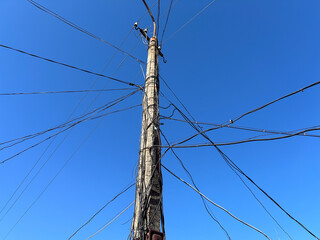 A utility pole stands in a city with many wires extending in different directions. The sky is blue with no clouds