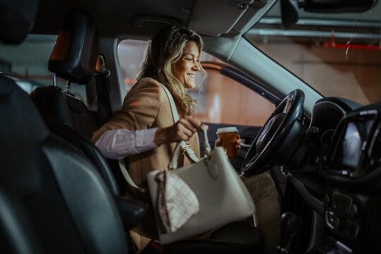 Professional woman getting into her car in a parking garage with coffee and a handbag, preparing for her morning commute