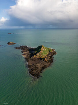 Aerial view of the rugged island, a dark jewel embraced by the tranquil turquoise sea under a cloudy sky, Pleneuf-Val-Andre, Brittany, France.