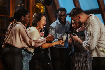 Diverse friends celebrating together, a man pouring champagne into glasses, women smiling and...