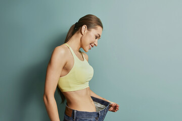 Woman smiles while holding oversized pants in front of green wall during indoor activity showcasing...