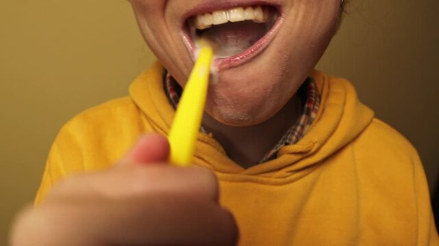 Close-up of a person brushing teeth with yellow toothbrush and white foam. Dental hygiene, oral care, and morning routine concept. Young woman cleaning teeth