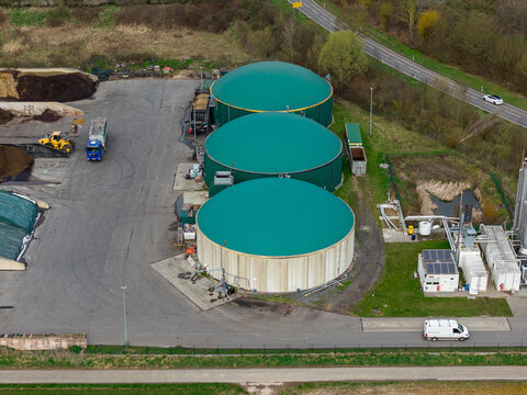 Aerial view of circular biogas plant tanks with green roofs stand starkly against the landscape, Gross-Umstadt, Hessen, Germany.
