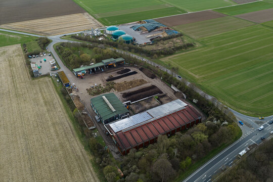 Aerial view of a composting plant in the foreground and biogas plant in the back with containers, green fields, and brown soil under a cloudy sky, Gross-Umstadt, Hessen, Germany.