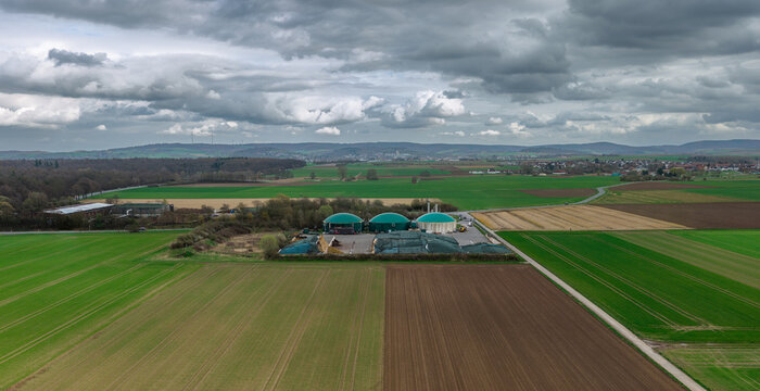 Aerial view of a Biogas plant gleams amidst the patchwork quilt of green and brown fields under a vast, brooding sky, Gross-Umstadt, Hessen, Germany.
