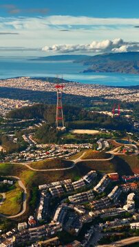 Iconic lattice radio tower situated on a forested hilltop with a sprawling urban landscape and ocean in the distance. Sutro Tower on a green hill overlooking city. Vertical video.