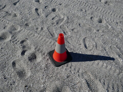 Isolated orange traffic cone on beach sand with footprints and tire tread marks around