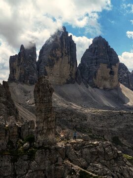 Aerial view of the majestic Tre Cime di Lavaredo peaks piercing the sky, their rugged surfaces contrasting with soft, ethereal clouds, Tre cime Lavaredo, Italy.