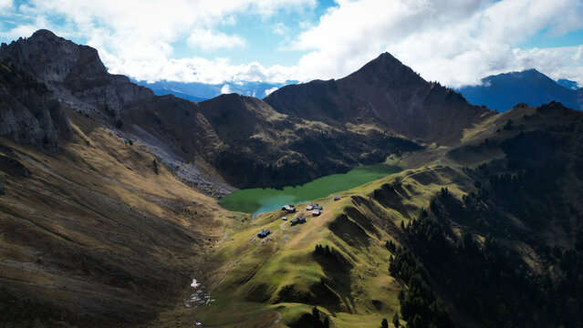 Aerial view of jagged peaks and verdant slopes embrace a tranquil lake nestled beneath the towering Pic de Jallouvre, Glieres-Val-de-Borne, Auvergne-Rhone-Alpes, France.