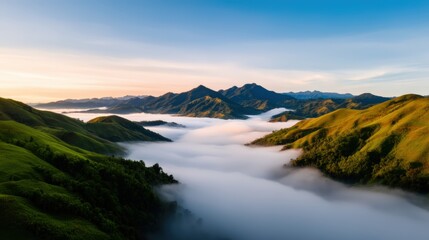 Obraz premium A stunning landscape featuring rolling green hills and majestic mountains, shrouded in a blanket of fog beneath a clear, blue sky.