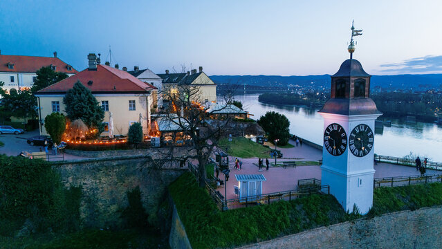 Aerial view of the iconic clock tower and fortress walls overlooking the tranquil Danube River under the fading twilight sky, Petrovaradin, Vojvodina, Serbia.