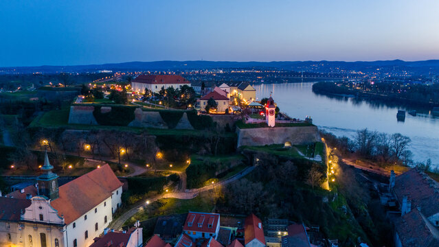Aerial view of the illuminated Petrovaradin Fortress standing majestically above the Danube River, a beacon of history against the twilight sky, Petrovaradin, Vojvodina, Serbia.