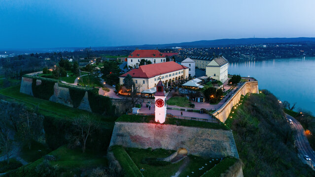 Aerial view of the illuminated clock tower and fortress walls meet the dark waters of the Danube river, Petrovaradin, Vojvodina, Serbia.