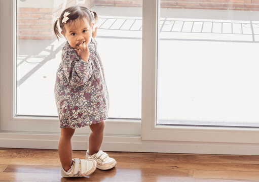Shy toddler girl standing by window during first day of preschool orientation