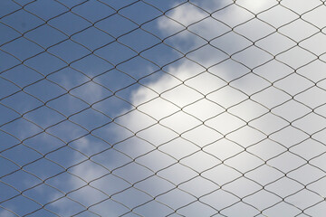 Siatka ochronna z drutu na tle błękitnego nieba i chmur, geometryczny wzór rombów, bariera i zabezpieczenie. © Henryk Guziak