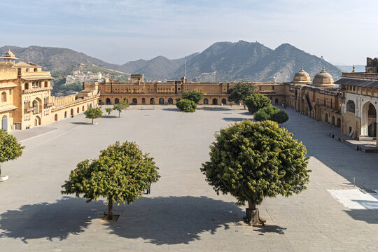 View of the expansive courtyard, framed by the amber-hued walls of Amer Fort and distant mountains, a blend of nature and architecture, Jaipur, Rajasthan, India.