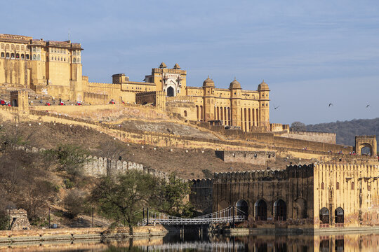 View of the majestic Amber Fort rises with honeyed walls, echoing history above the tranquil lake in Amber Fort, Jaipur, Rajasthan, India.