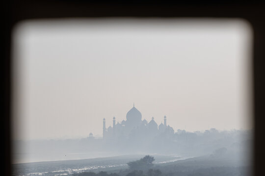 View of the Taj Mahal's ethereal silhouette through a stone window, a dreamy vision in soft grays and muted whites, framed by the ancient architecture, Agra, Uttar Pradesh, India.