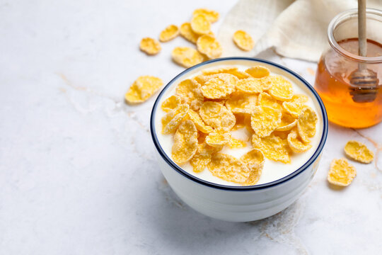 Tasty corn flakes with milk in bowl served on white marble table, closeup. Space for text