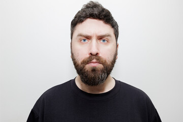 Fototapeta premium A straightforward frontal headshot of a serious man with a thick beard and blue eyes on a white background. Stock photo