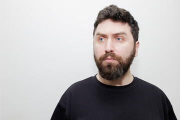 Fototapeta premium A minimalist portrait of a bearded man wearing a black sweatshirt, looking away against a neutral white background. Stock photo