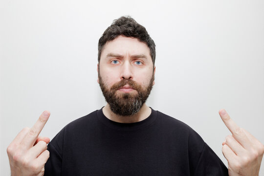A portrait of an expressive man with a beard showing the middle finger gesture against a white studio background. Stock photo