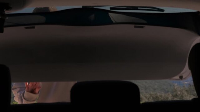 Adventurous female hiker getting backpack from car trunk. View from inside a car as a woman opens the trunk, takes out her backpack, and prepares for a hike in the mountains overlooking a sea
