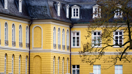 Bright yellow royal-style castle stands prominently with towers and ornate facade details. The warm colored walls contrast with the sky and surrounding greenery, giving the building a fairytale, regal © Василий Канин