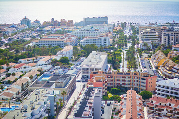 Obraz premium Elevated city and coastline view of Los Cristianos in Tenerife, Canary Islands, Spain. Sunny resort district with hotels, apartment buildings, palm trees, and Atlantic Ocean shoreline
