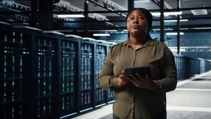 Fototapeta premium Data center engineer using app on tablet to ensure error free rigs networks for intense computational demands. Worker monitoring server hub equipment components for failures, camera A