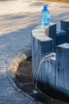 An outdoor drinking fountain with running water and a plastic bottle on a stone pedestal. Mineral water spring