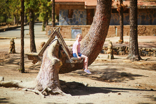Little girl sitting on a rustic wooden bench built into a curved pine tree in Las Lajas, Tenerife, Canary Islands, Spain.